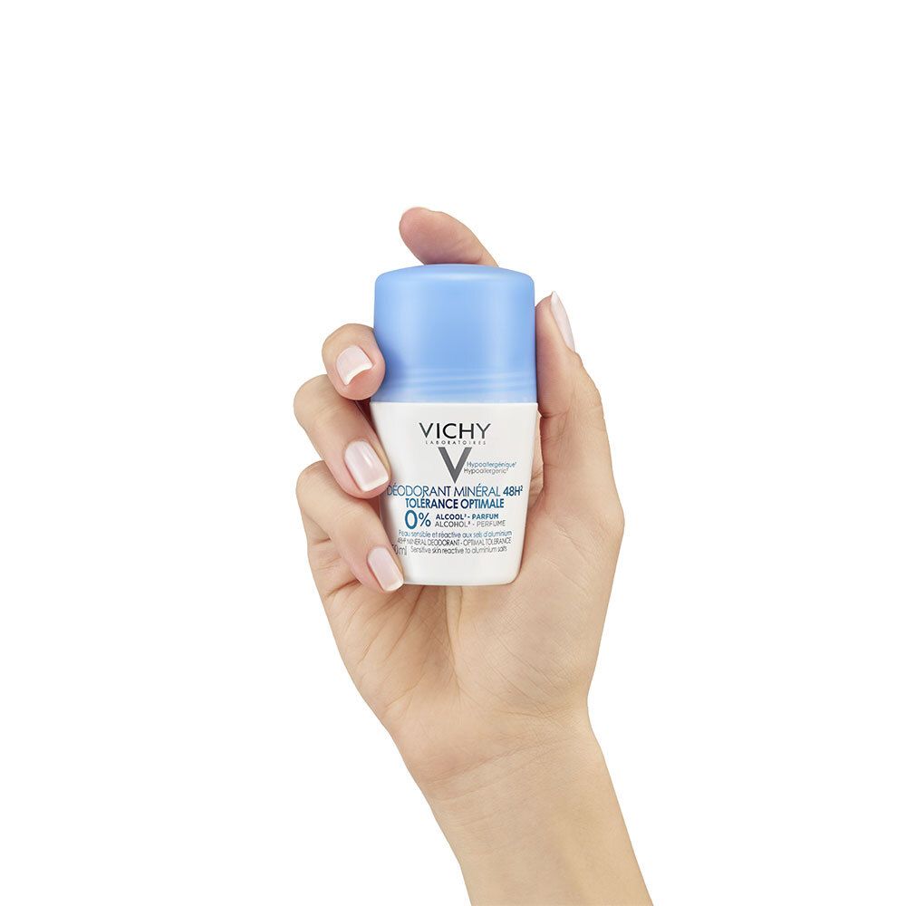 Main tenant un déodorant roll-on. Contenant blanc, bouchon bleu. Texte: VICHY, 0% alcool.