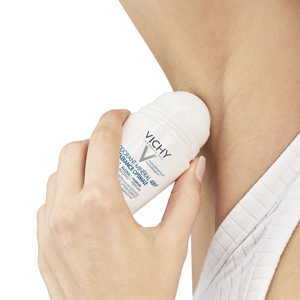 Personne appliquant un déodorant roll-on sous l'aisselle. Contenant blanc, bouchon bleu.
