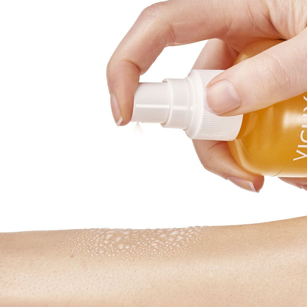 Main vaporisant du spray solaire sur un bras. Liquide jaune vaporisé. Tête de pulvérisation blanche.