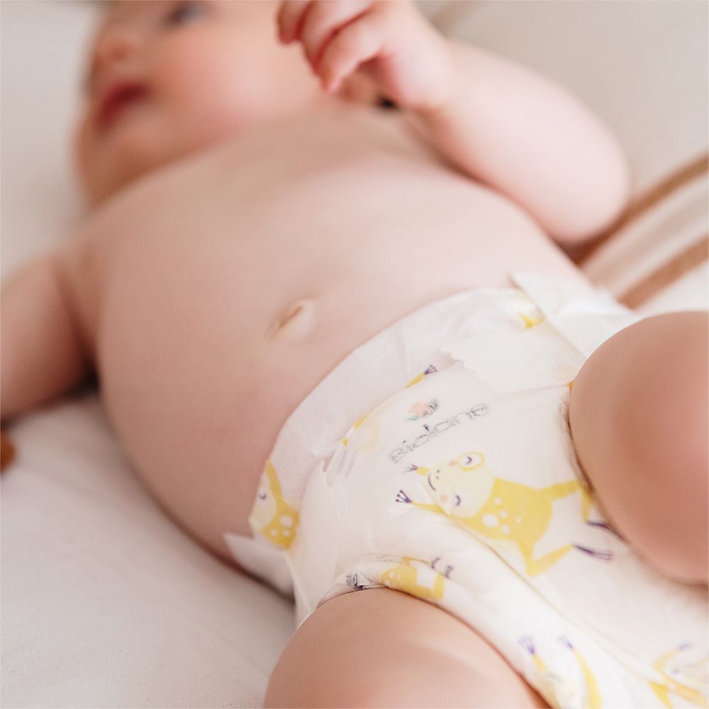 Bébé portant une couche Biolane Bio taille 1. Motif grenouille jaune. Couche couvrant le ventre.