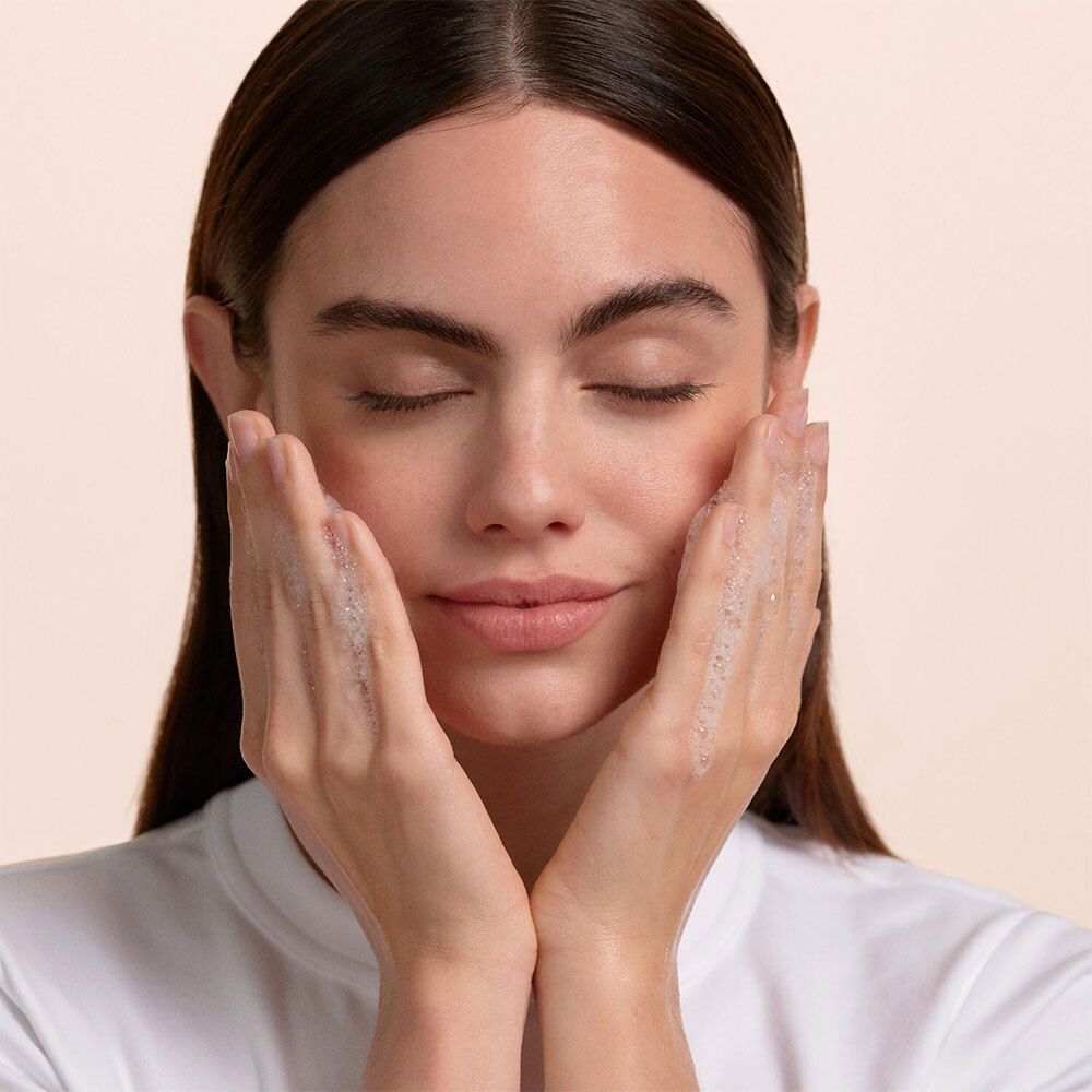 Femme aux yeux fermés, mains couvertes de savon. Aucune indication de produit visible.