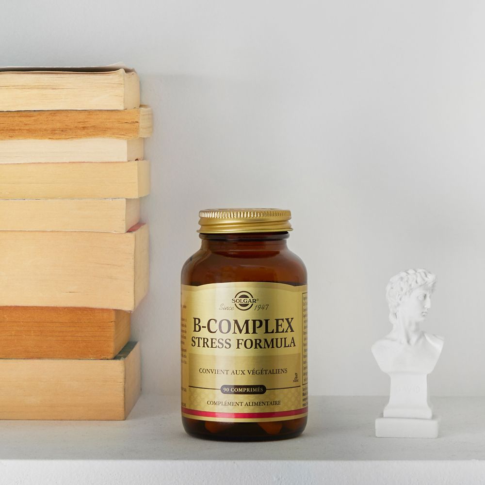 Flacon en verre brun avec bouchon doré. Étiquette SOLGAR, B-Complex Stress Formula, 90 comprimés. À côté de livres.