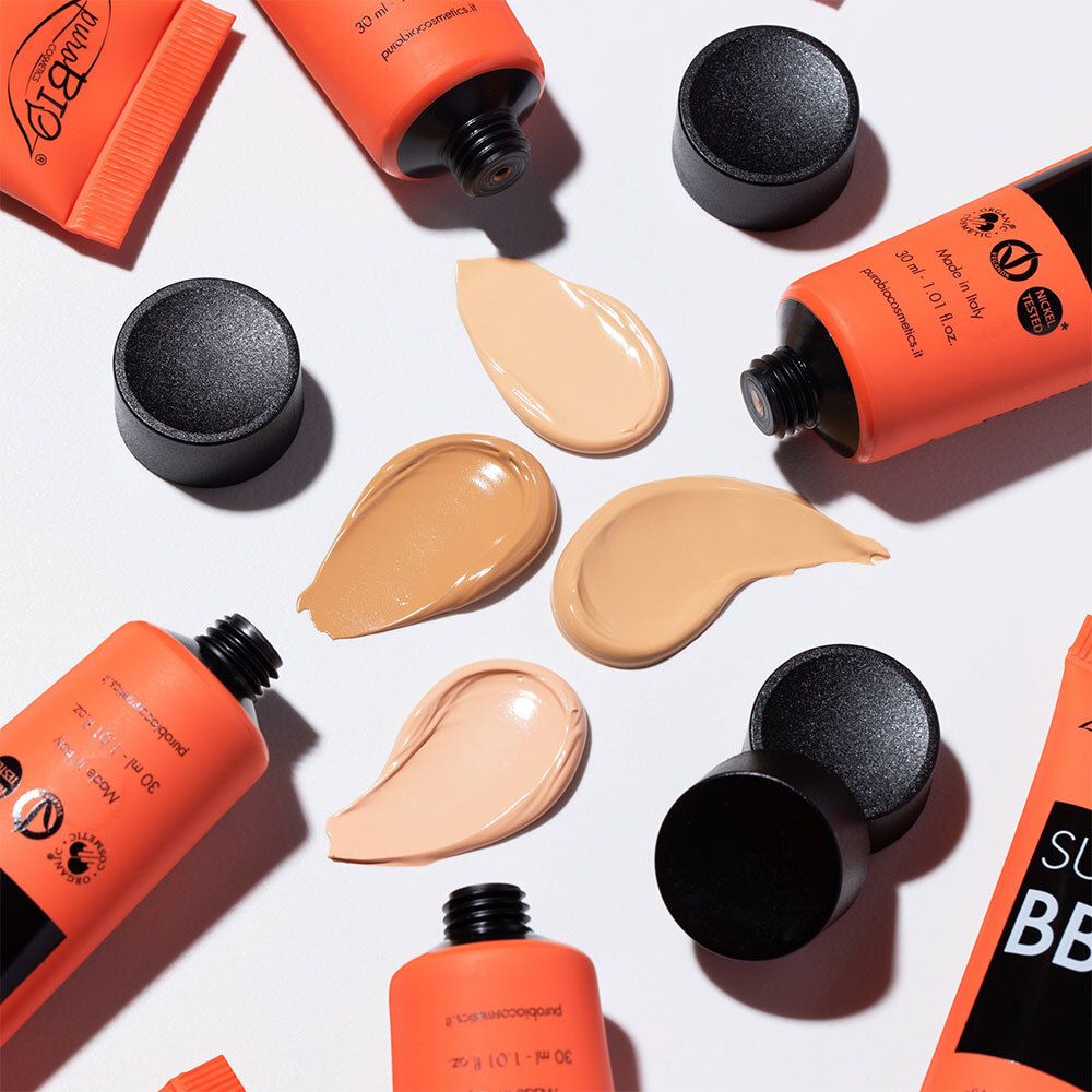 Plusieurs tubes et échantillons de BB cream. Tubes orange avec bouchon noir. Échantillons de différentes teintes.