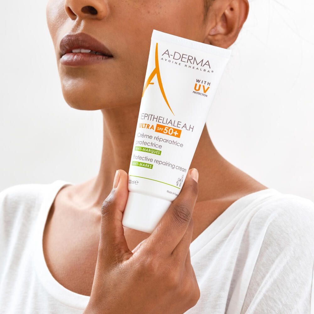 Femme tenant un tube A-DERMA EPITHELIALE A.H. ULTRA LSF 50+. Produit en main.