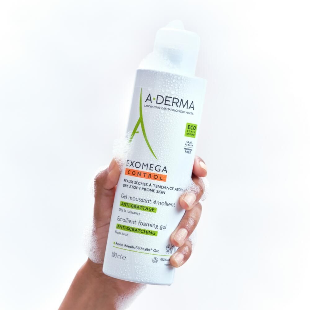 Hand hält A-DERMA EXOMEGA CONTROL Gel. Schaum um die Flasche. Produkt für trockene, zu Ekzemen neigende Haut.