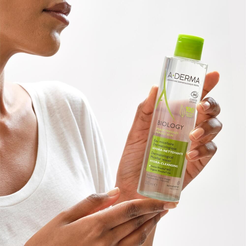 Personne tenant un flacon d'eau micellaire A-DERMA BIOLOGY. Flacon avec bouchon vert. Inscription: Biology, Hydra-Cleansing.