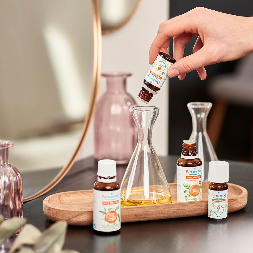 Mains tenant des flacons. Plusieurs flacons sur un plateau. Étiquettes : Tea Tree. Autres flacons et décoration.