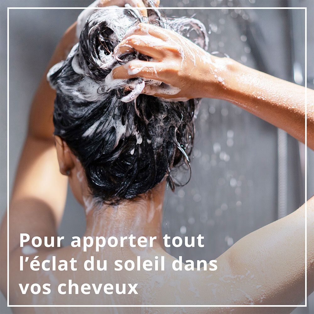 Personne se lave les cheveux sous la douche. Texte: 'Pour apporter tout l'éclat du soleil dans vos cheveux'.
