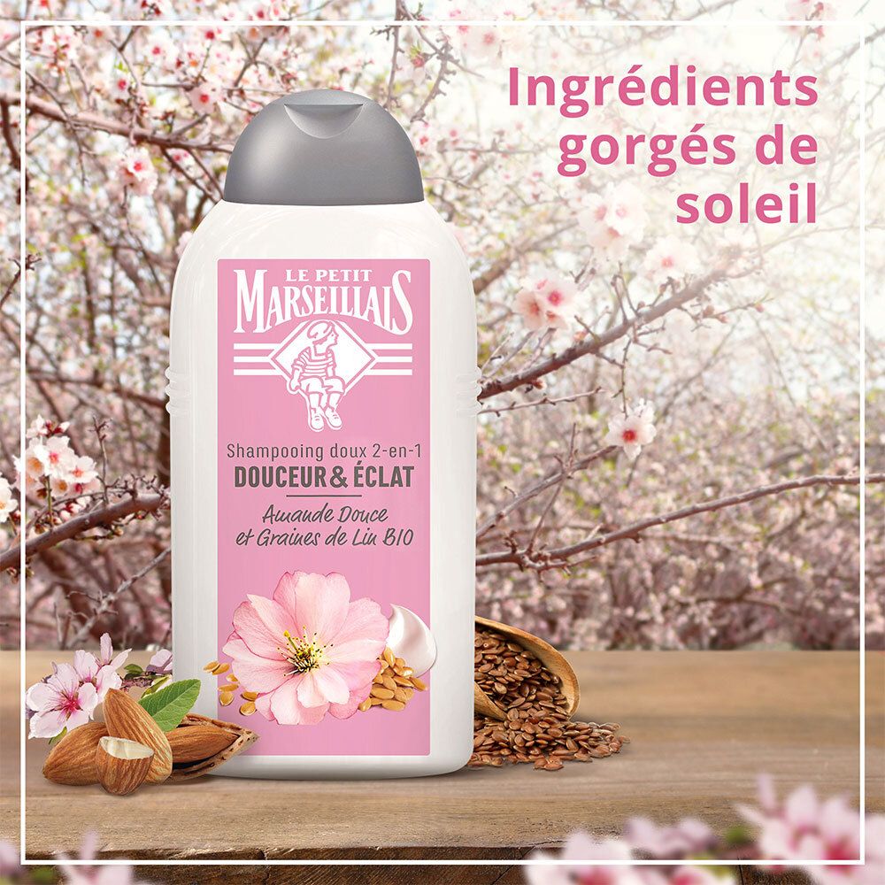 Le Petit Marseillais Shampooing doux 2-en-1. Flasche vor Blütenzweigen und Zutaten. Text: Douceur & éclat, Ingrédients gorgés de soleil.