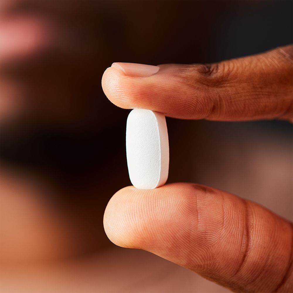 Un comprimé blanc ovale tenu entre deux doigts.