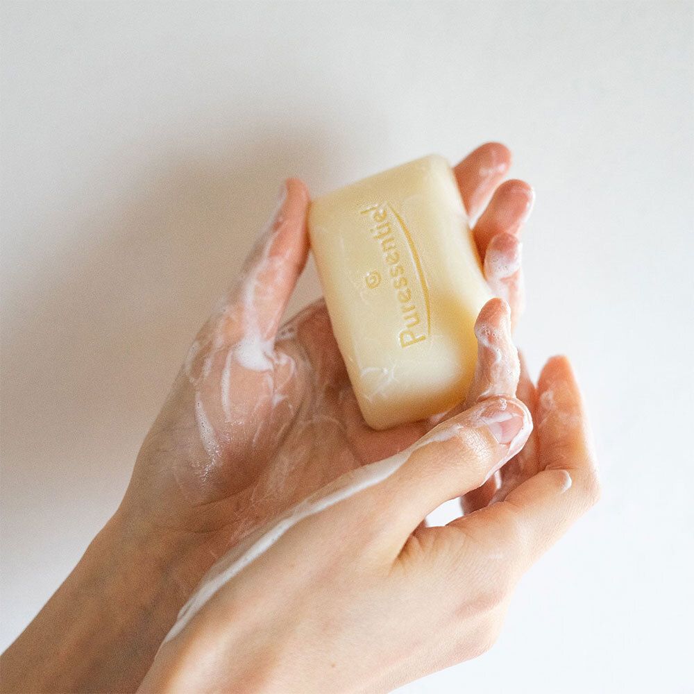 Mains avec mousse de savon, pain de savon. Inscription : Puressentiel.