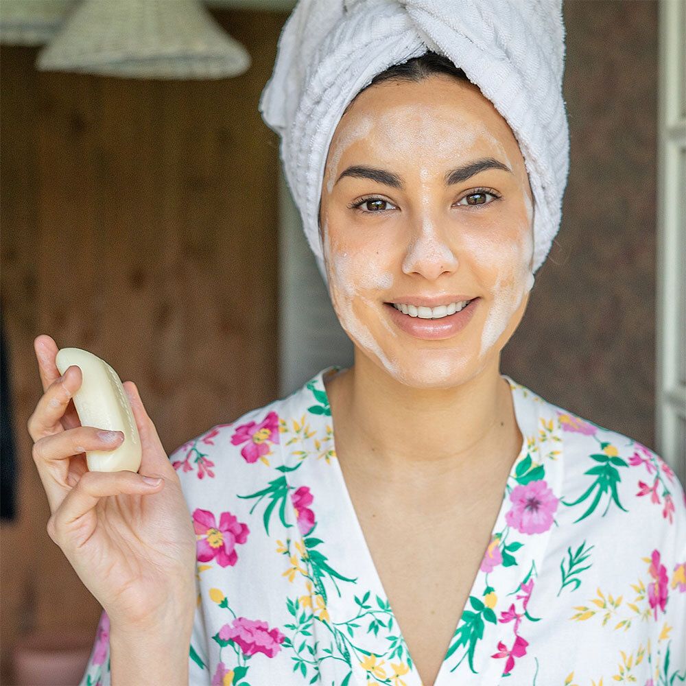 Femme avec serviette et savon. Visage avec mousse de savon. Inscription : Puressentiel.