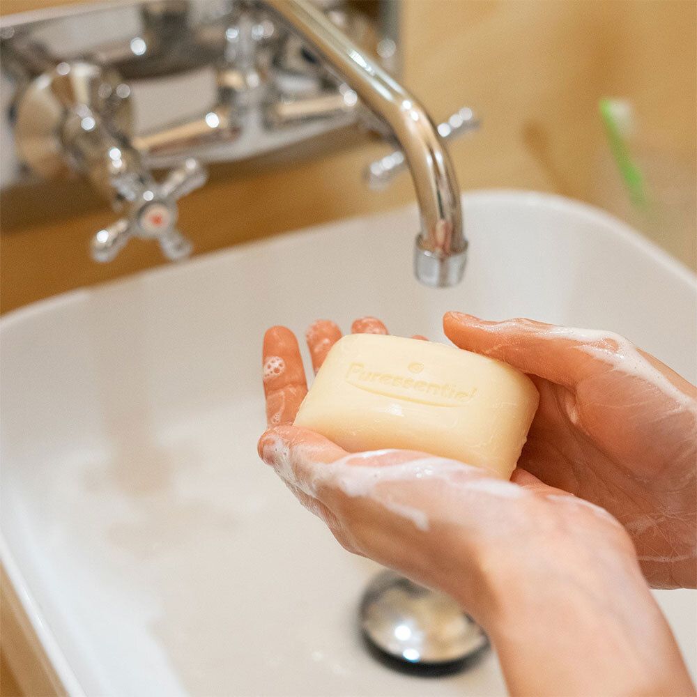Mains sous robinet, pain de savon et mousse. Inscription : Puressentiel.