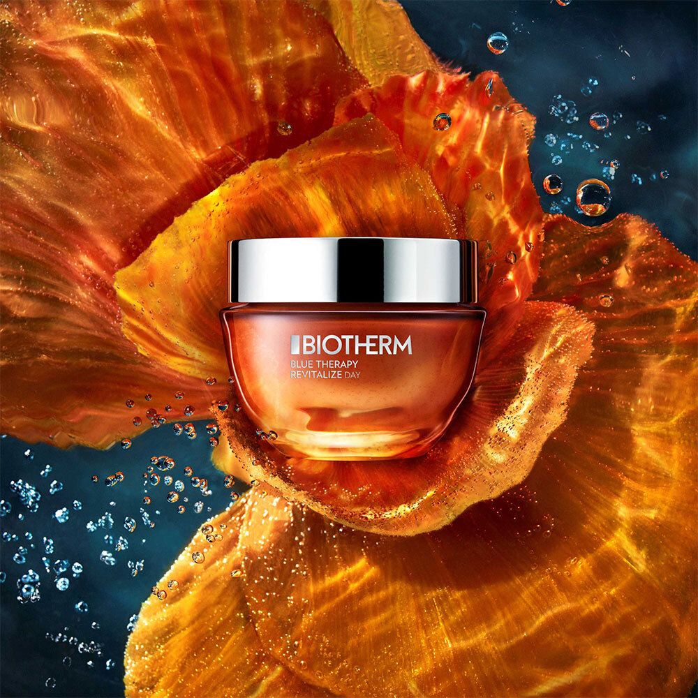 Creme-Tiegel in orangefarbener Blüte. Aufschrift BIOTHERM BLUE THERAPY REVITALIZE DAY.