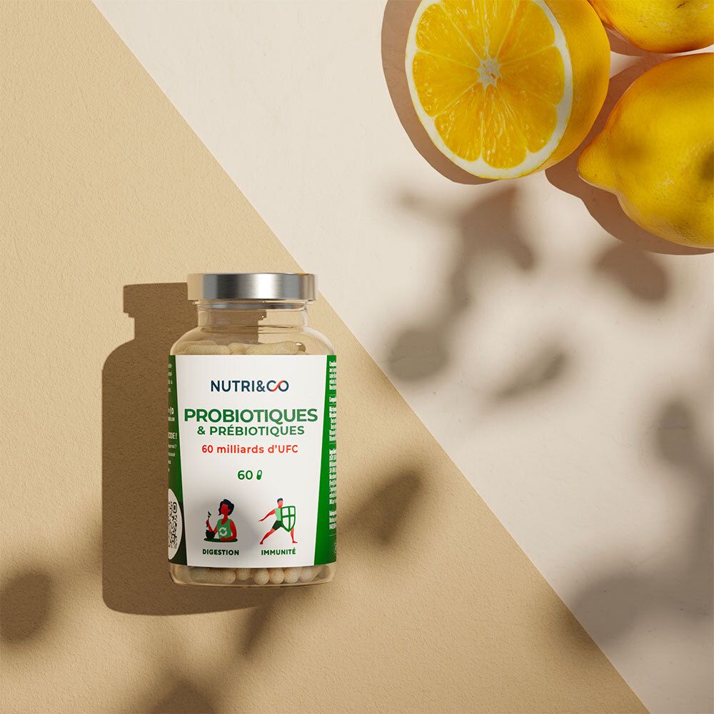 Flacon avec gélules près de citrons. Étiquette NUTRI&CO, Probiotiques & Prébiotiques, 60 milliards UFC. Sur fond clair.