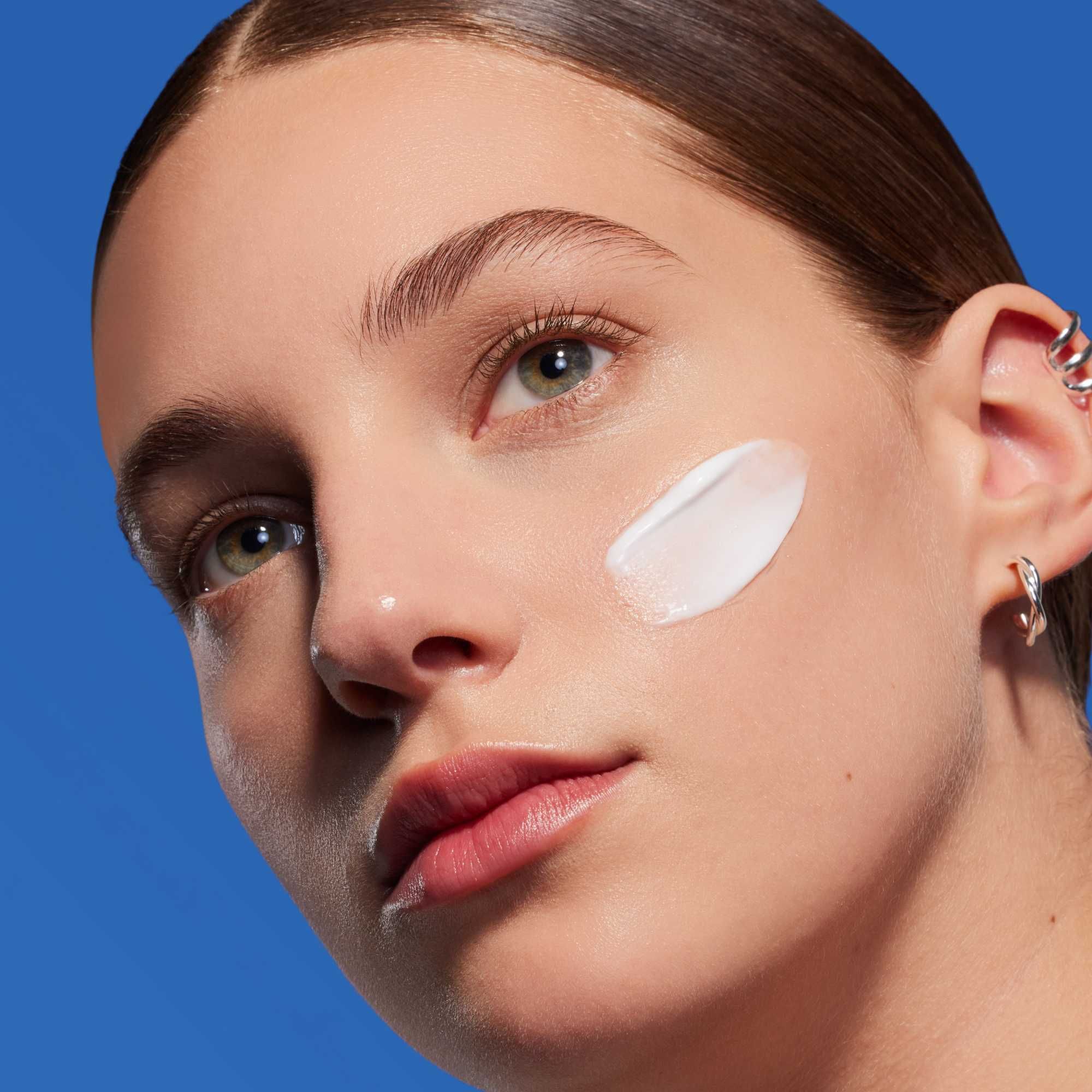 Visage d'une femme avec crème sur la joue. Fond bleu.