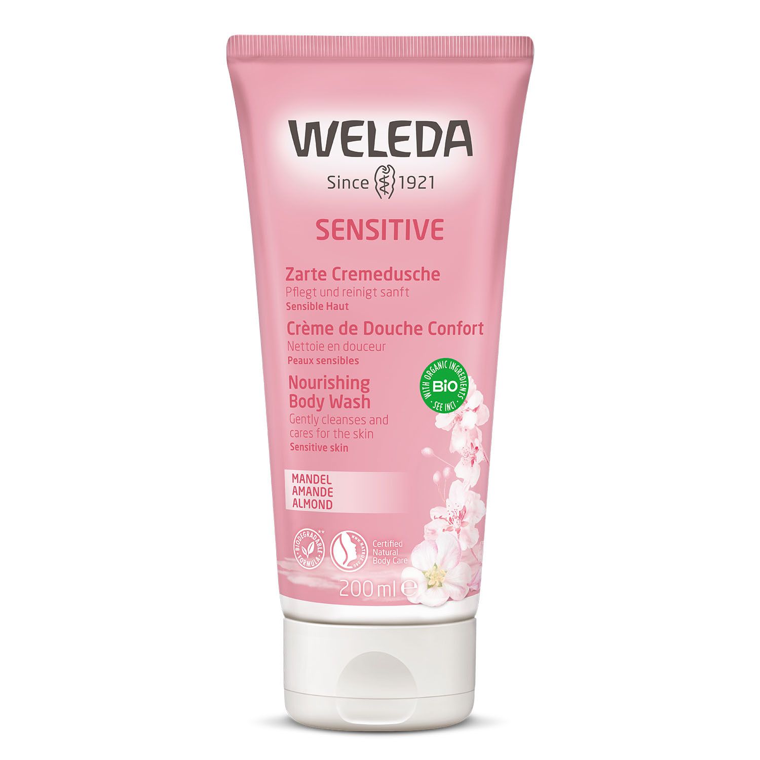 Tube rose "WELEDA". Inscriptions "Sensitive" et "Crème de Douche Confort". Logo bio. Fleurs d'amandier en illustration.