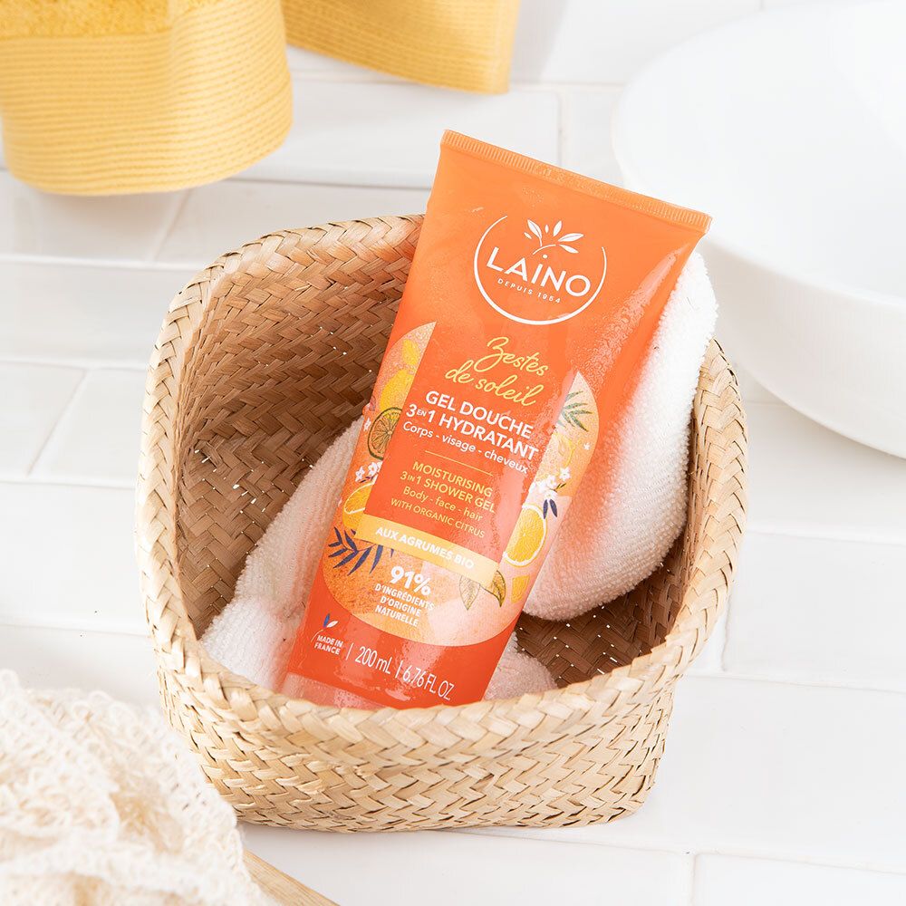 Orangefarbene Tube in einem geflochtenen Korb mit Handtuch. Produktname und Logo deutlich sichtbar. Hintergrund: Bad-Arrangement.