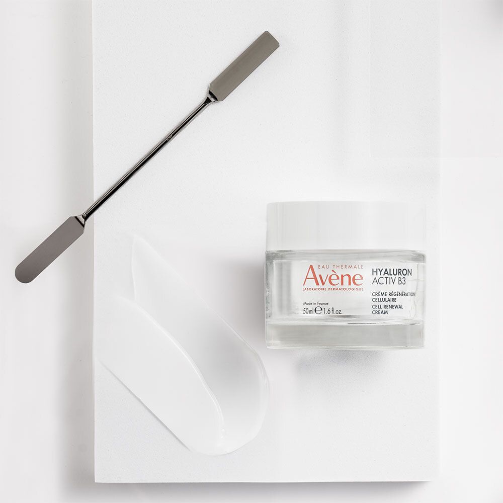 Pot de crème, spatule et bandes de crème sur fond blanc. Nom du produit non visible.