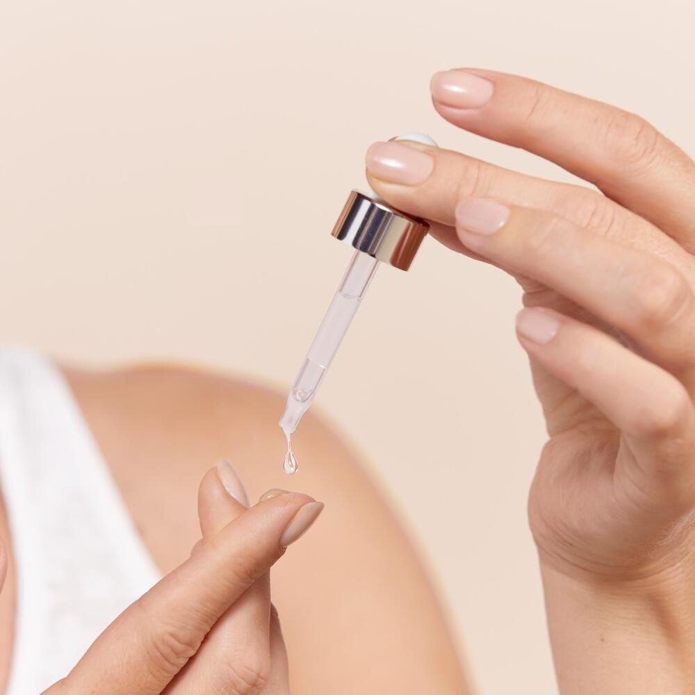 Mains tenant une pipette avec du sérum. Une goutte de sérum sur le doigt.