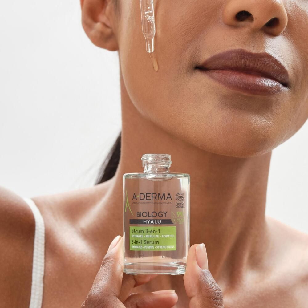 Femme avec sérum 3-en-1 A-DERMA BIOLOGY HYALU. Goutte sur la peau. Flacon en verre transparent.