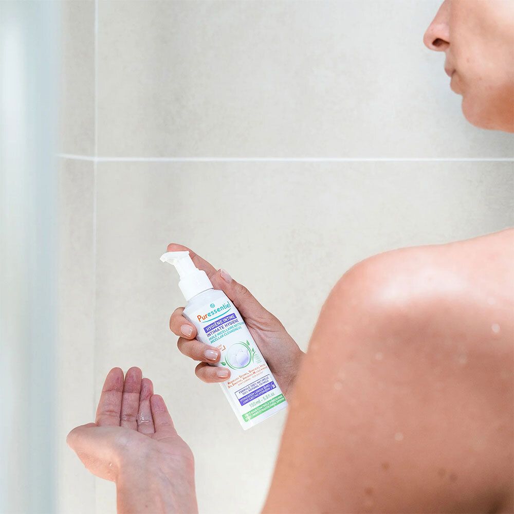 Personne tenant un flacon blanc avec pompe. Inscription : Puressentiel, Hygiène Intime. Personne sous la douche.