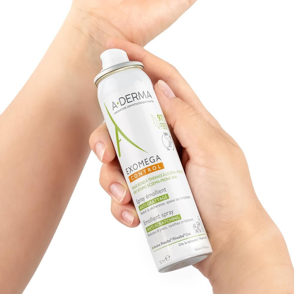 Mains tenant le spray A-DERMA EXOMEGA CONTROL. Flacon blanc, bouchon vert. Texte visible.