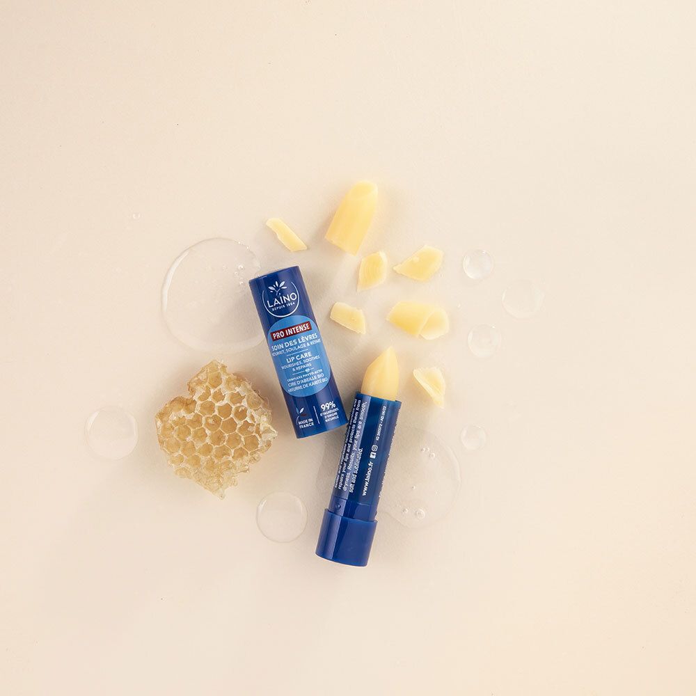 Zwei blaue Lippenpflegestifte mit LAINO-Logo, daneben Honigwabe und Wachsstücke. Auf cremefarbenem Hintergrund.