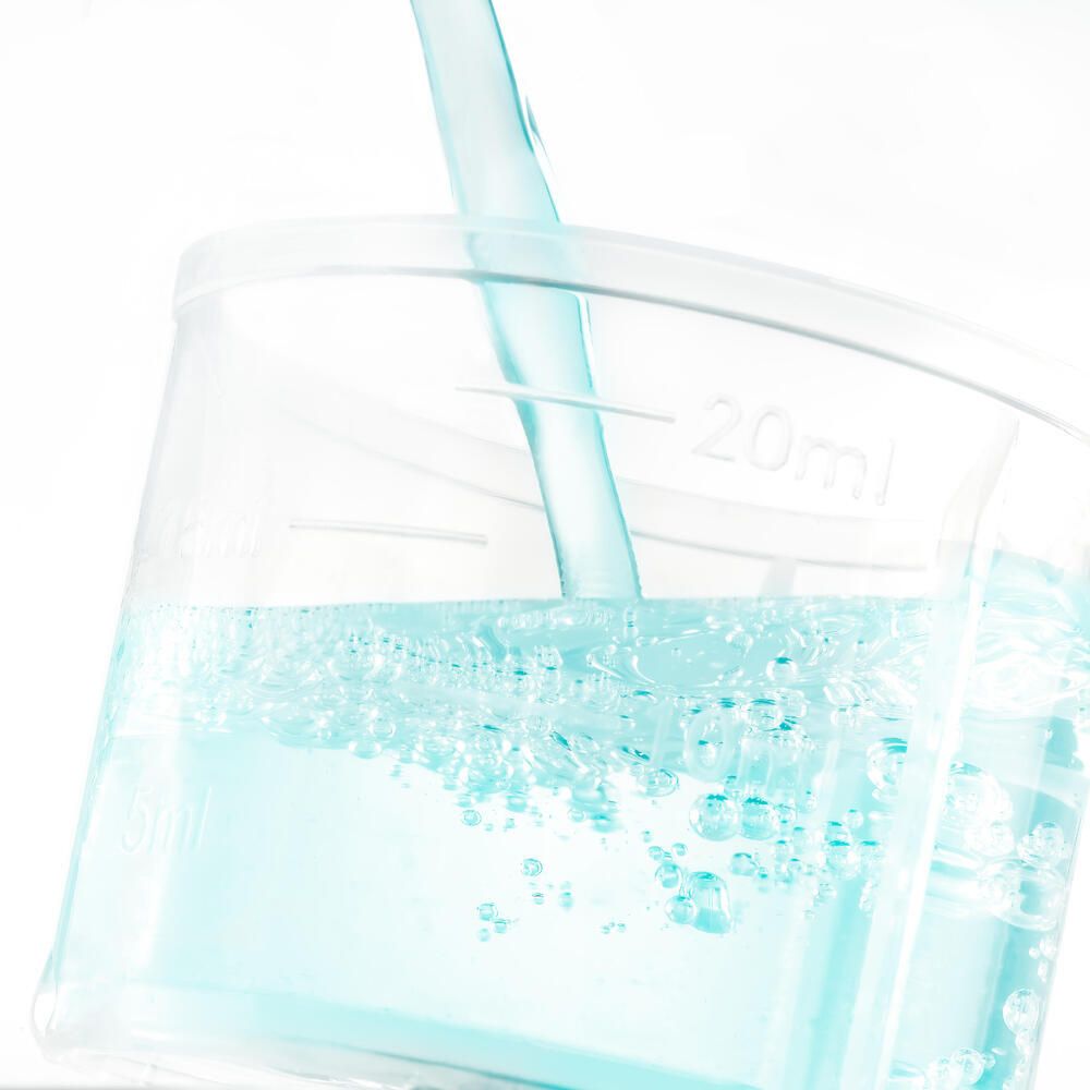 Gobelet doseur avec liquide bleu versé d'une bouteille. Échelle de 20 ml. Plastique transparent.