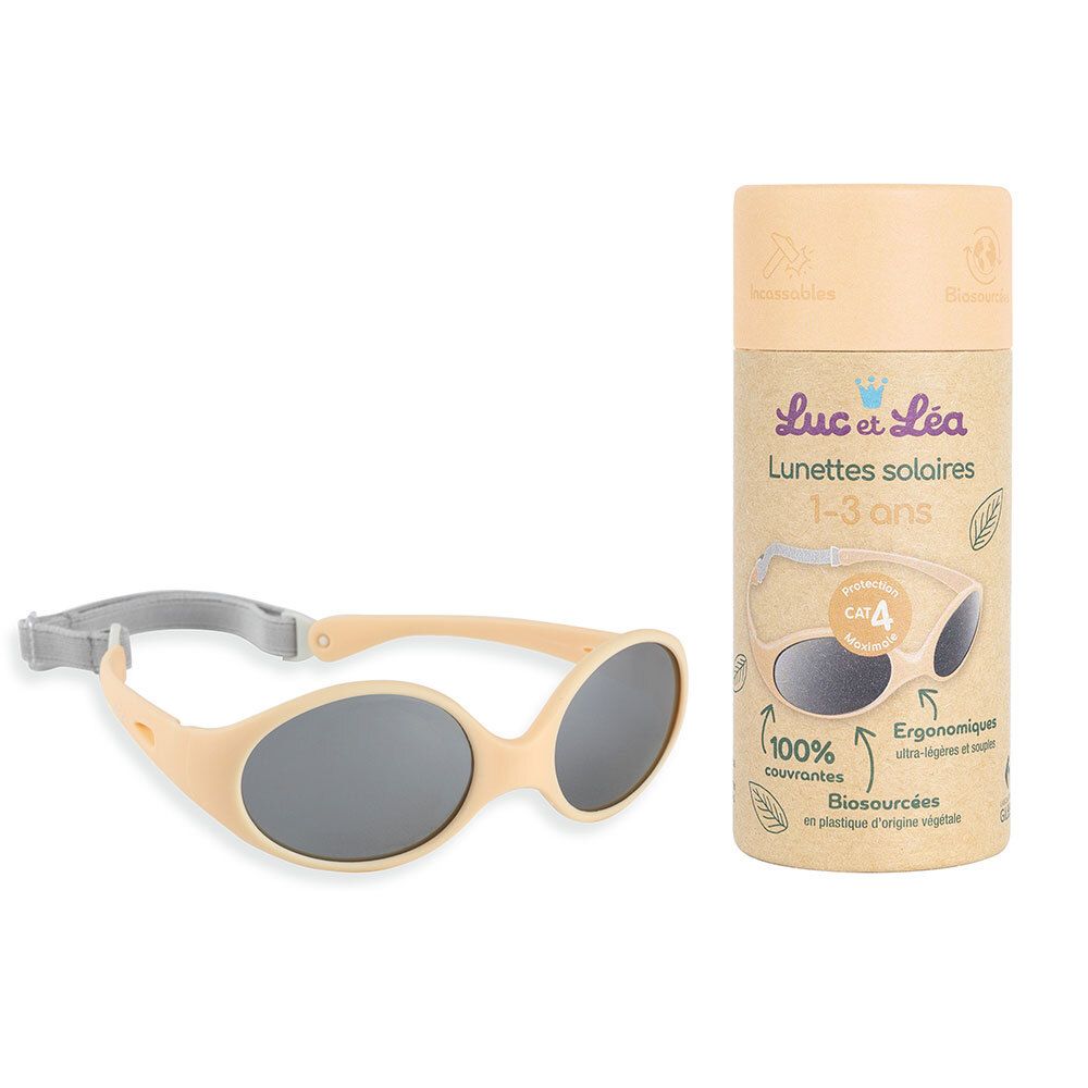 Lunettes de soleil beiges avec verres gris et bandeau gris. À côté, l'emballage. Inscription: Luc & Léa, lunettes de soleil 1-3 ans.