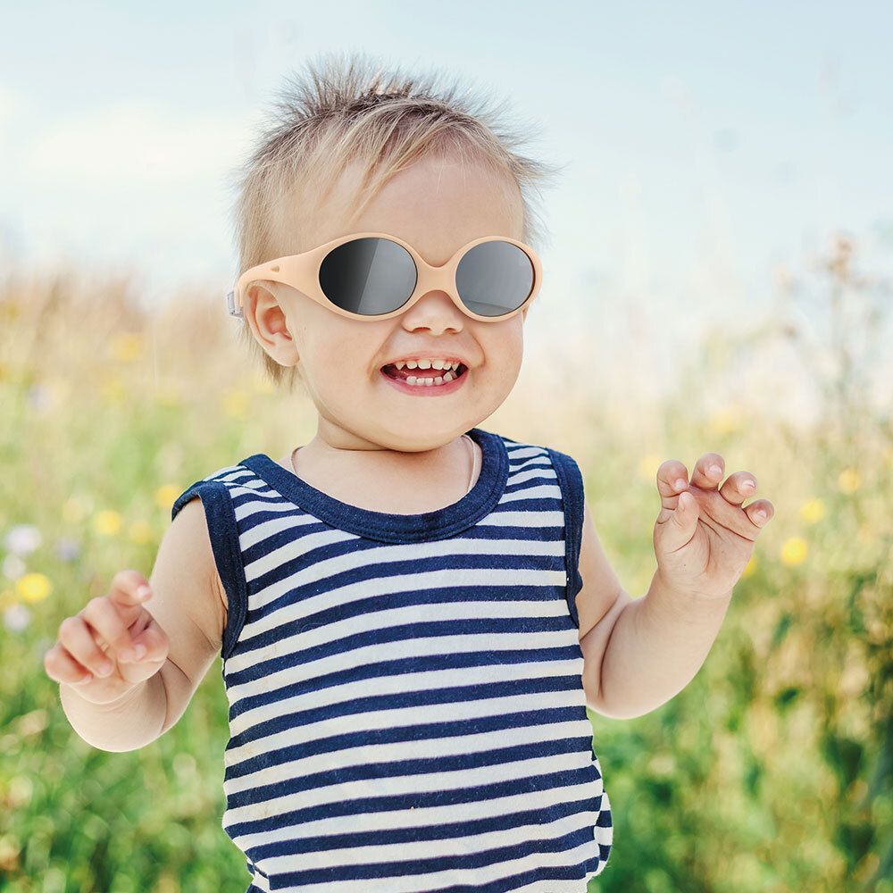 Jeune enfant portant des lunettes de soleil beiges avec verres gris. L'enfant porte un débardeur rayé bleu et blanc.