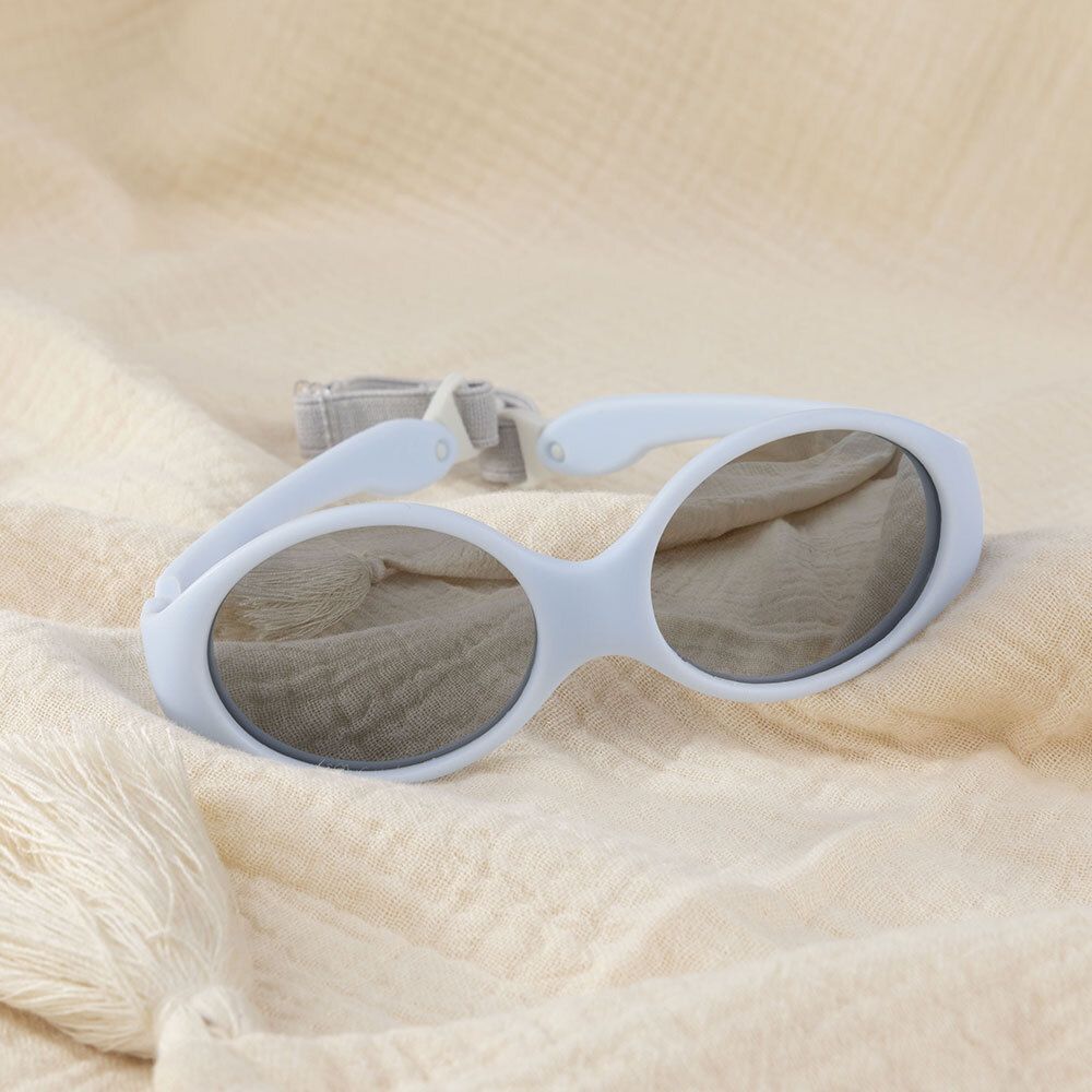 Lunettes de soleil bébé bleues sur tissu beige. Avec bandeau gris.