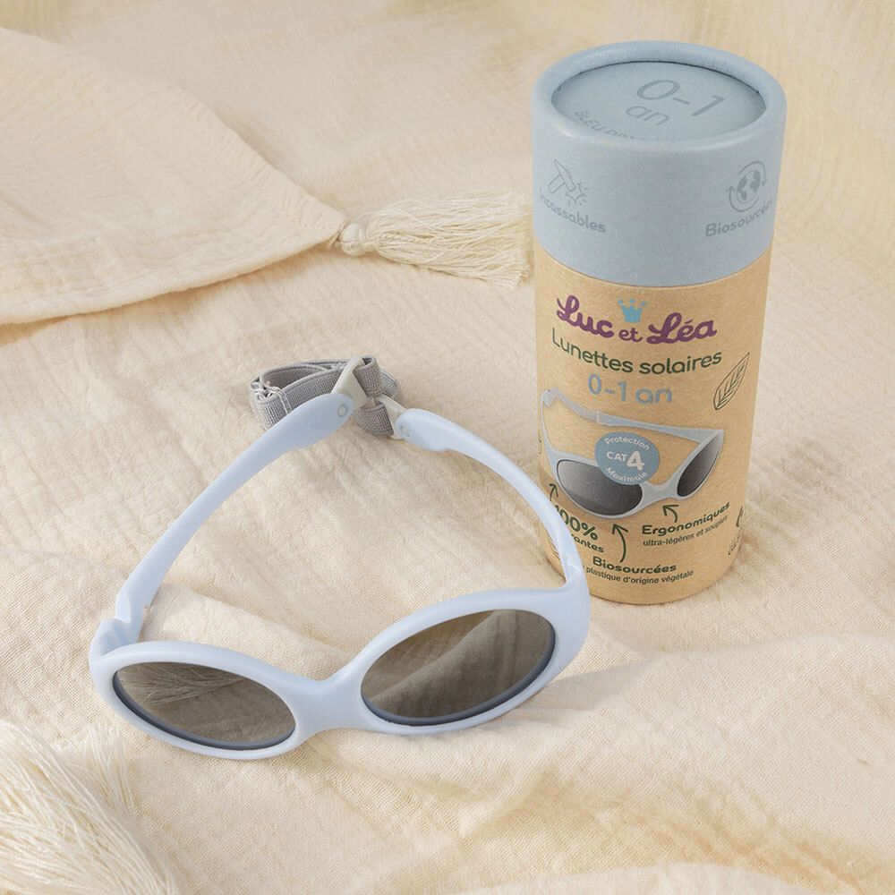 Lunettes de soleil bébé bleues, emballage et tissu. Texte : Luc et Léa, 0-1 an.