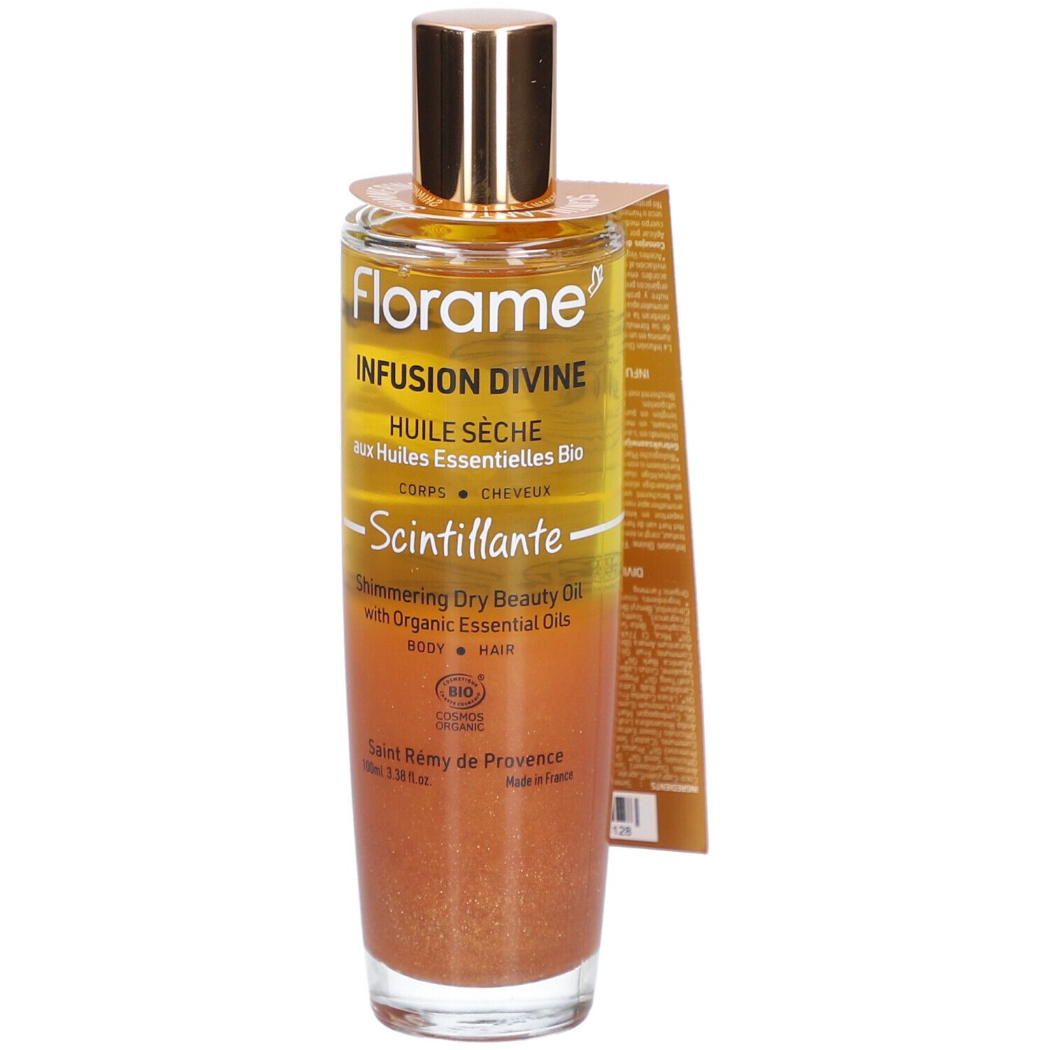 Flacon en verre avec bouchon doré. Étiquette avec nom et texte du produit. Liquide aux tons or et bronze.