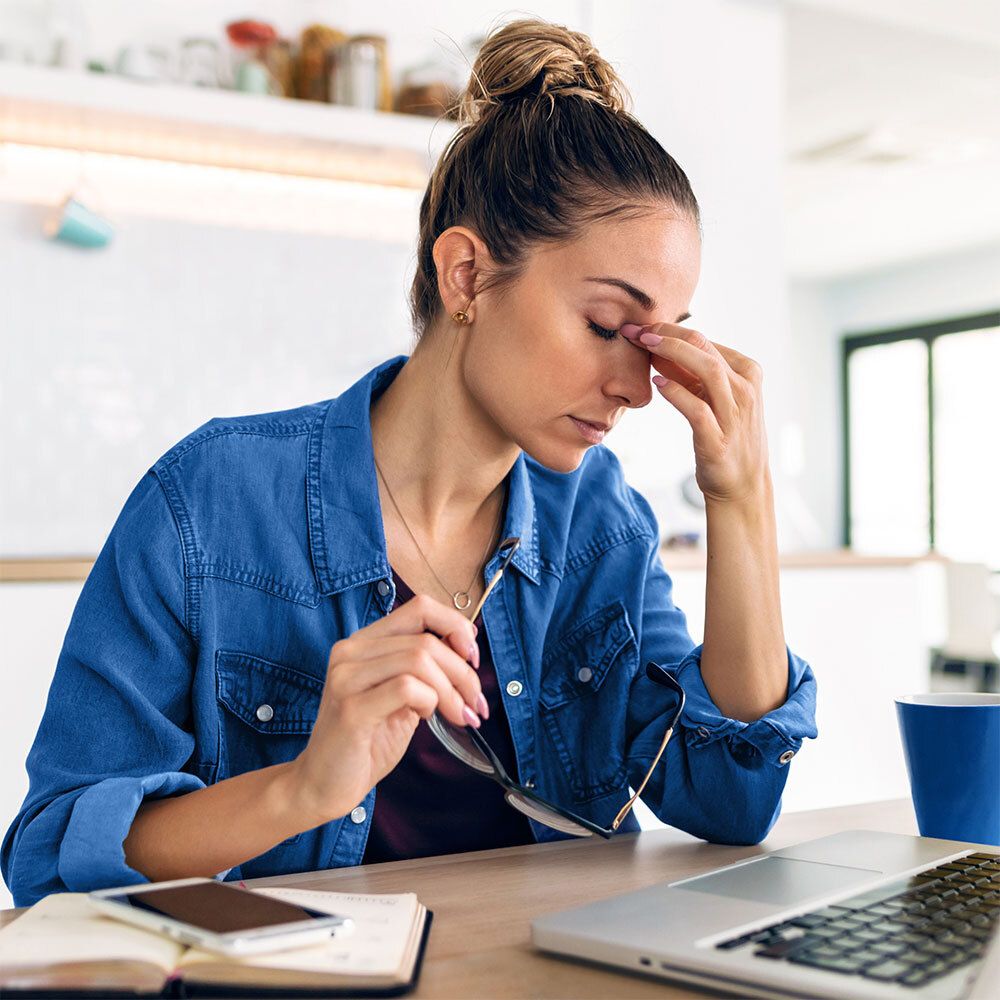 Frau mit Laptop. Sie berührt ihre Augen. Auf dem Tisch liegen eine Brille und ein Handy.