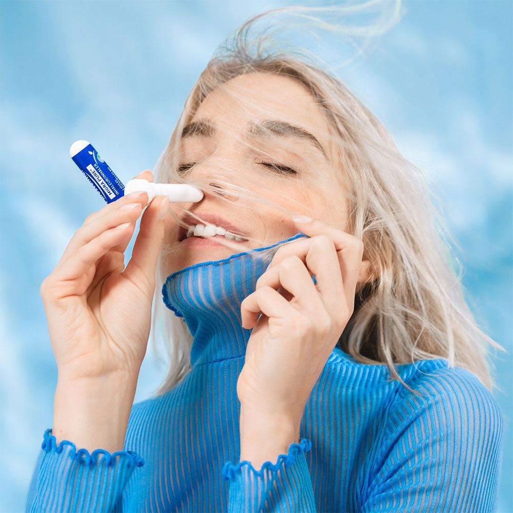 Frau mit Inhalator. Sie hält ihn an ihre Nase. Blauer Hintergrund.