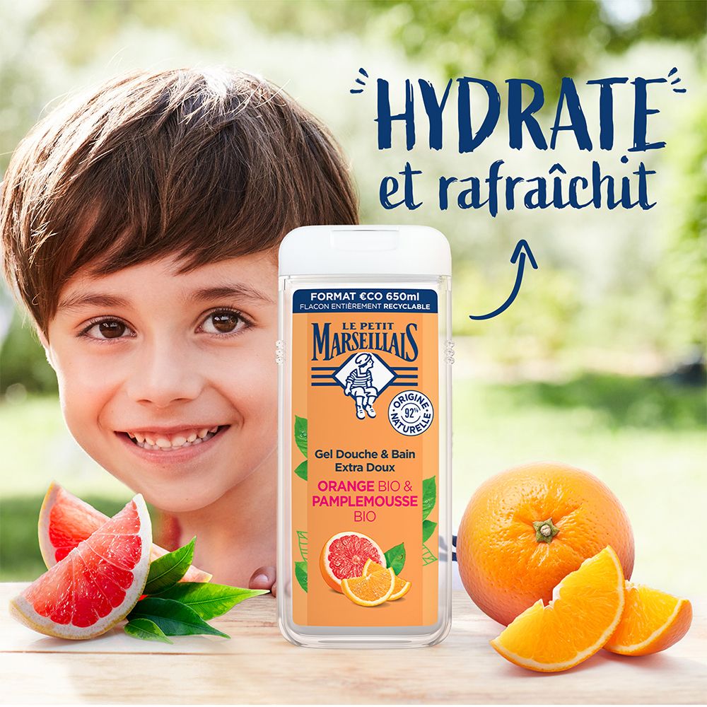 Kind lacht naast fles. Fles met oranje etiket. Tekst: Gel Douche & Bain Extra Doux Orange Bio & Pamplemousse Bio. Logo: Le Petit Marseillais.