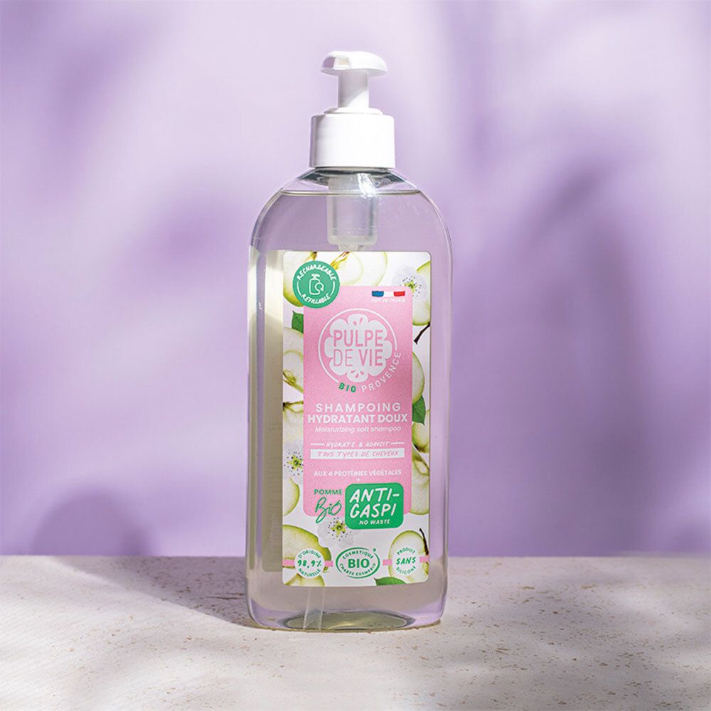 Flacon transparent avec pompe blanche. Étiquette avec nom du produit et illustrations de pommes. Fond violet.