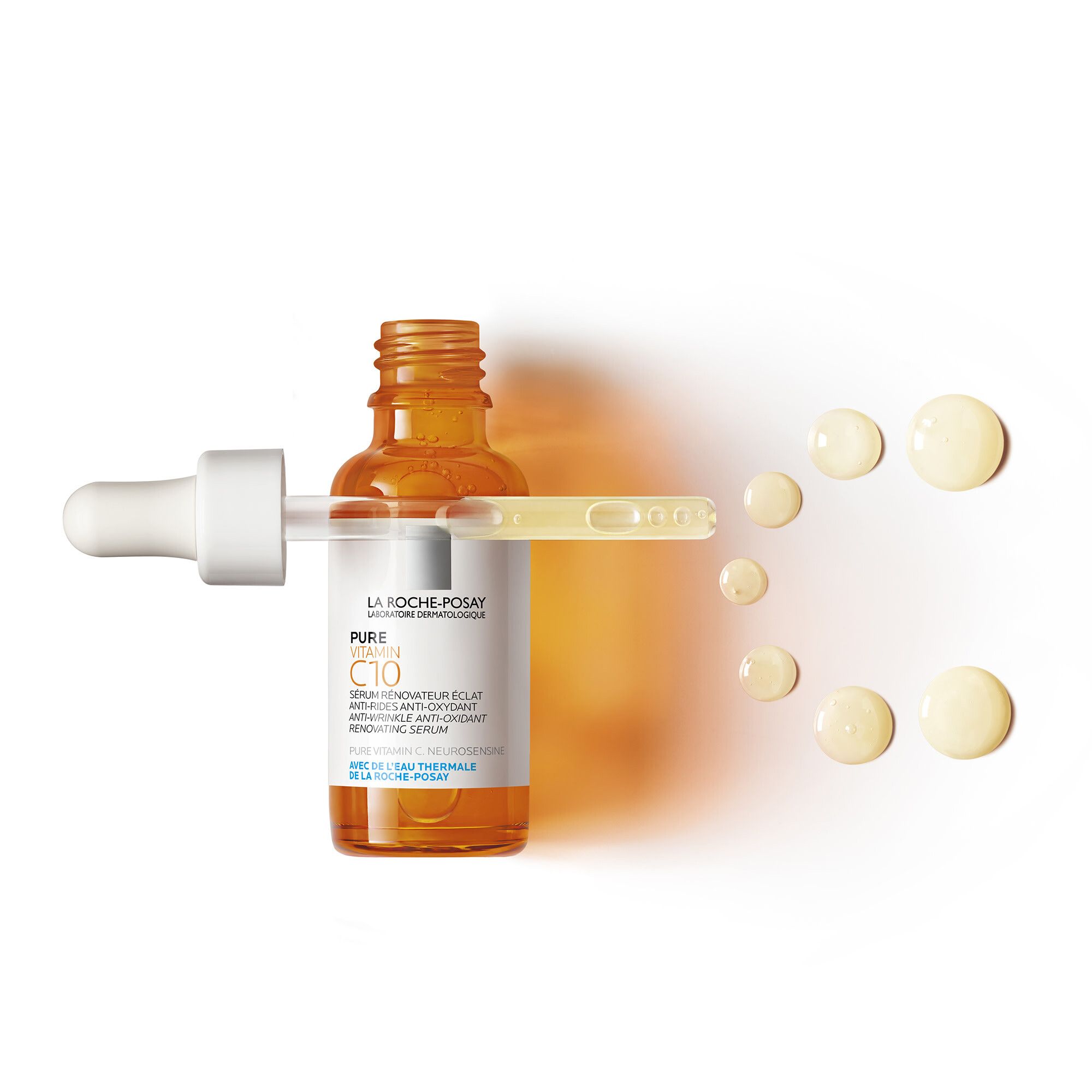 Flacon en verre ambré avec pipette et gouttes de sérum. Inscription: PURE VITAMIN C10 Sérum. Gouttes de sérum à côté.