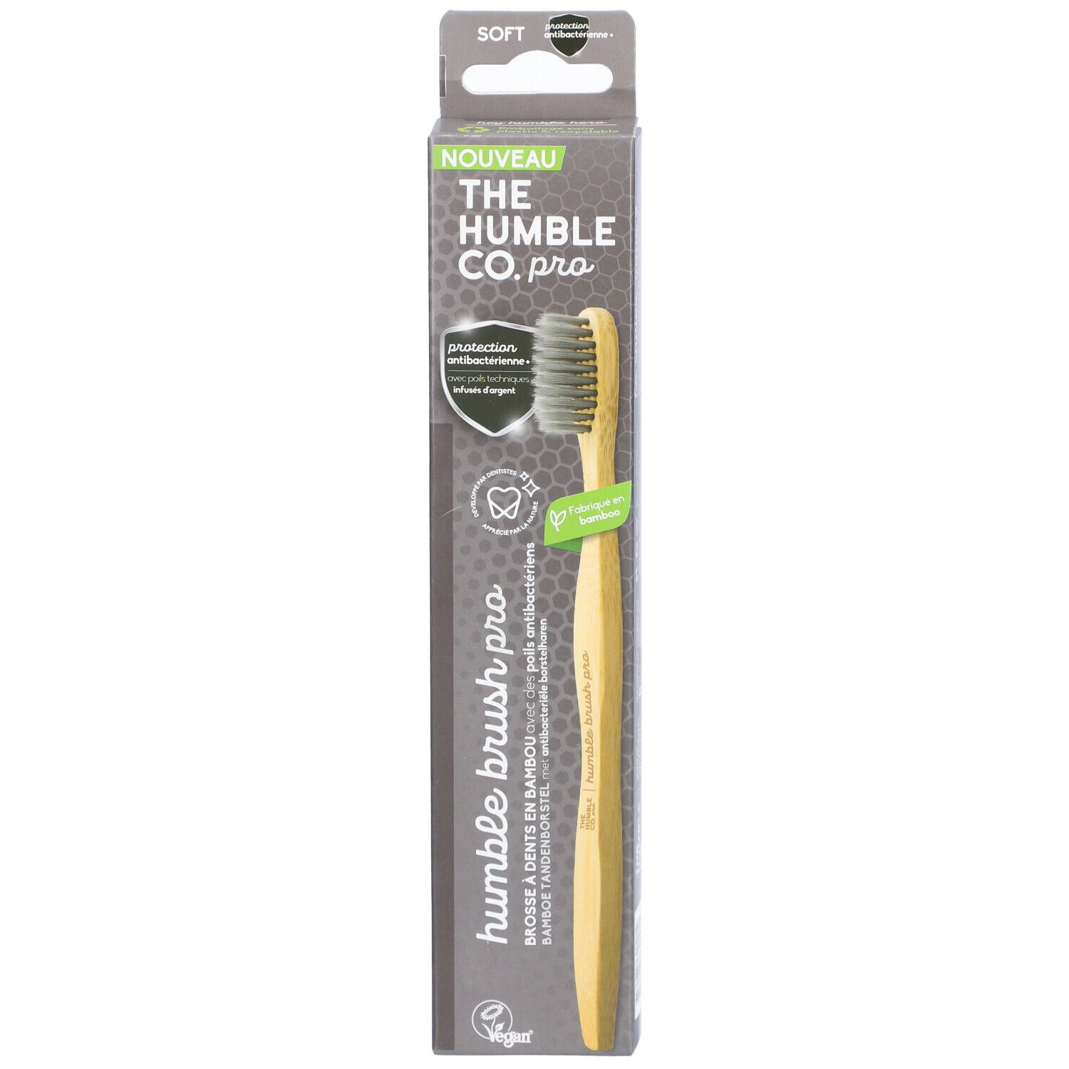 Brosse à dents dans son emballage. Manche en bambou, poils gris. Nom et logo du produit sur l'emballage.