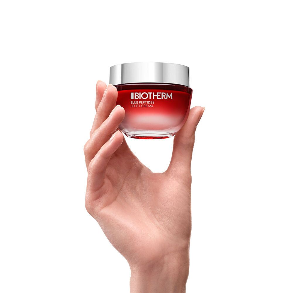 Main tenant un pot rouge avec couvercle argenté. Inscription : BIOTHERM, BLUE PEPTIDES.