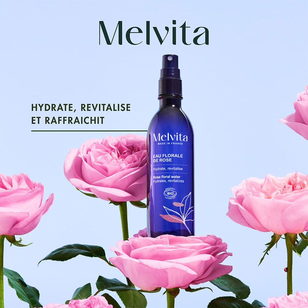 Melvita Rosenblütenwasserflasche umgeben von rosa Rosenblüten.