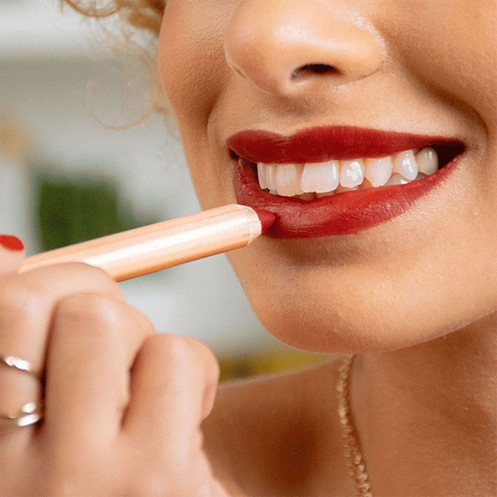 Nahaufnahme einer Person, die einen roten Lippenstift aufträgt. Sichtbare Lippen, goldene Halskette.