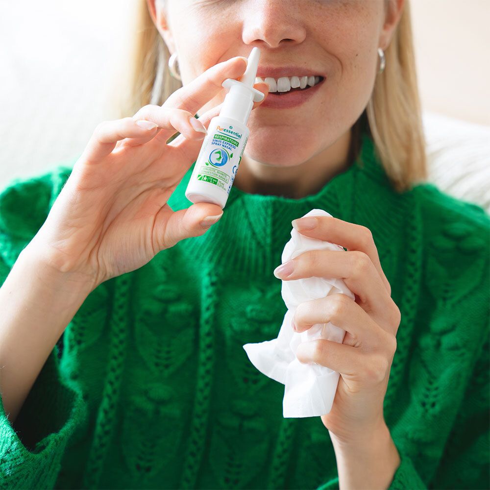 Femme tenant un spray nasal et un mouchoir. Inscription : Puressentiel Respiratoire Sinus Express Spray Nasal. La femme porte un pull vert.