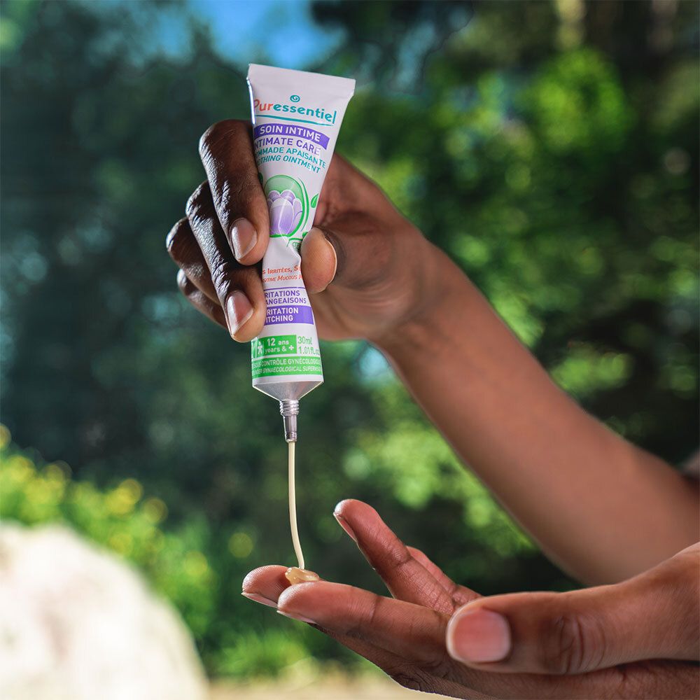 Main tenant un tube. Crème appliquée sur un doigt. Texte: Soin Intime Intimate Care. Pour irritations.