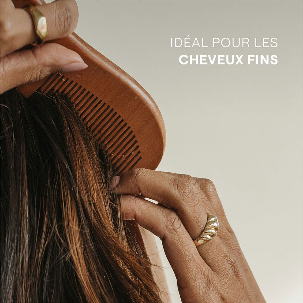 Main peignant les cheveux fins avec un peigne en bois. Bague dorée au doigt.