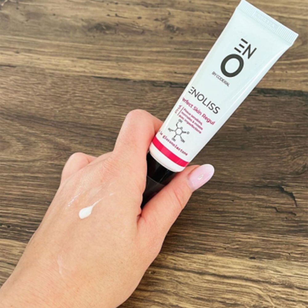 Hand houdt tube vast. Op de hand een kleine hoeveelheid crème. Opschrift: ENO, ENOLISS Perfect Skin Regul.