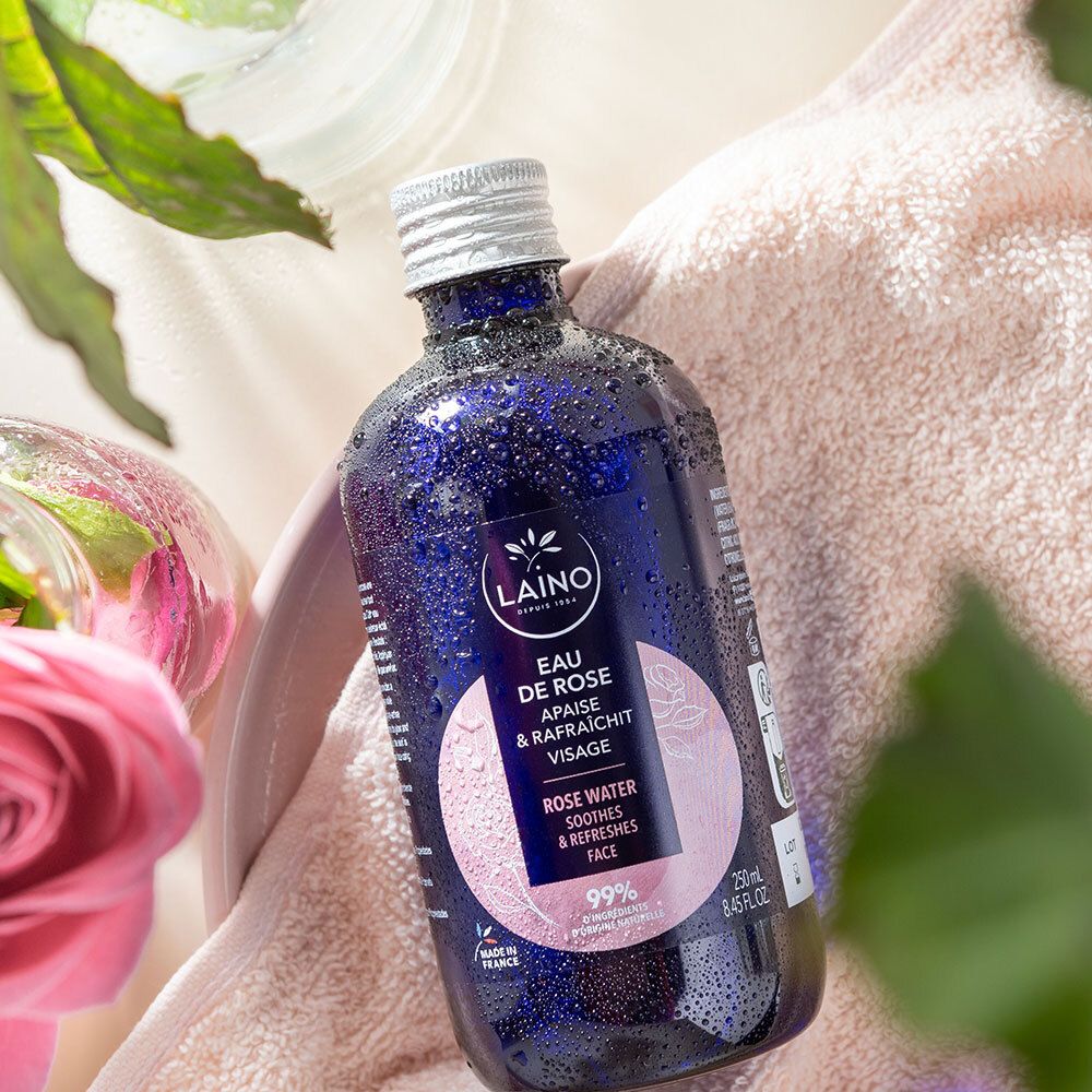 Eine Flasche LAINO Eau de Rose auf einem rosa Handtuch, umgeben von Rosen und Blättern.
