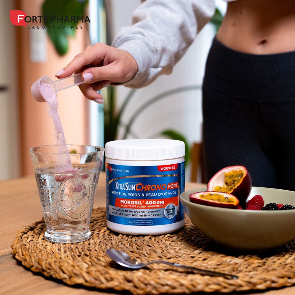 Personne verse de la poudre dans un verre. Pot XtraSlim Chrono Fort, fruits sur table. Forte Pharma.