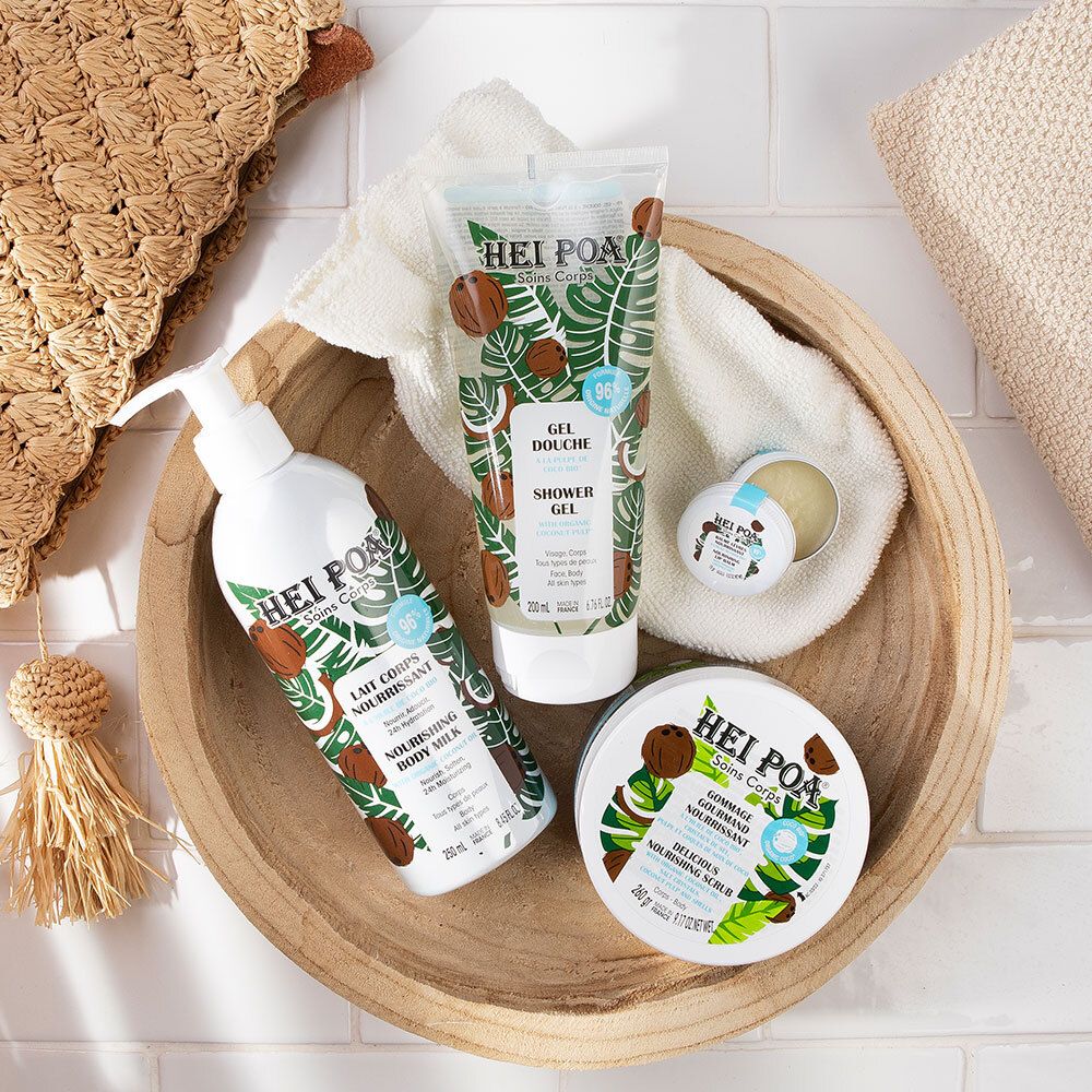 Holzschale mit Produkten: Duschgel, Body Milk, Creme. Kokosnuss- und Blattmuster. Text: HEI POA.